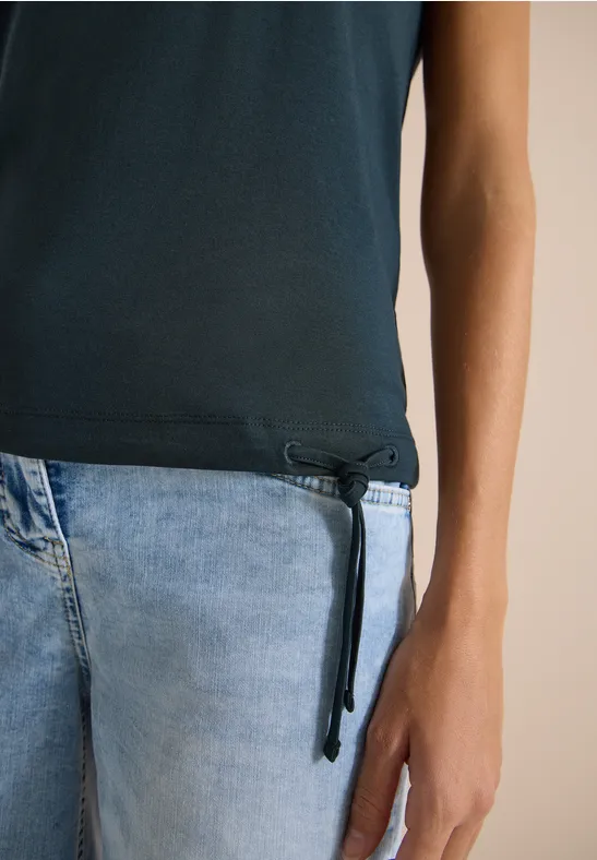 Ein Torso in dunkelblauem Shirt mit seitlicher Kordel und hellblauen Jeans.
