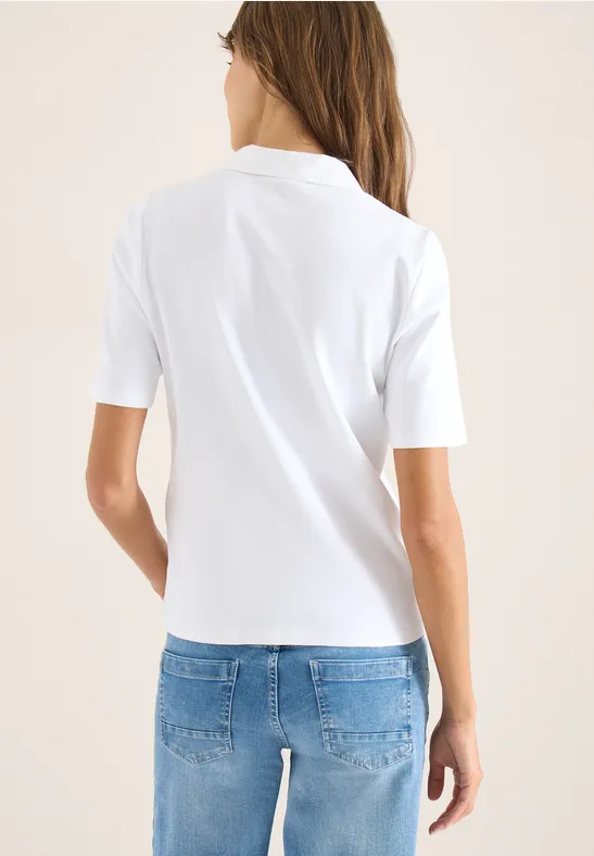 Eine Person steht mit dem Rücken zur Kamera, trägt ein weißes Poloshirt und blaue Jeans.