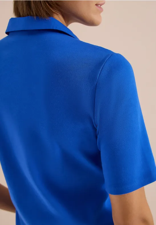 Eine Frau mit blauem Kurzarmshirt, Rücken und Teil des Gesichts sind sichtbar.