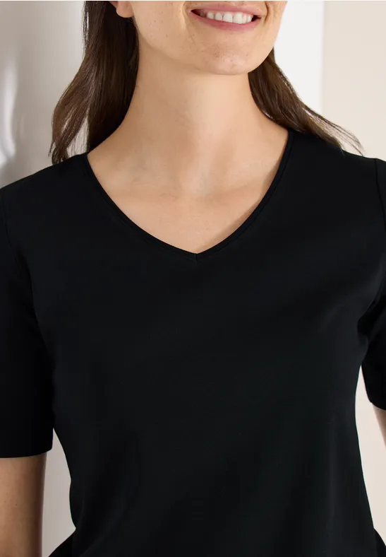 Eine Frau trägt ein schwarzes T-Shirt mit V-Ausschnitt. Sichtbar von Schultern bis Oberkörper.