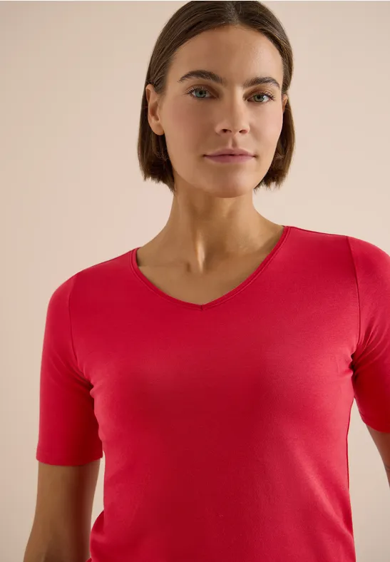 Frau mit rotem V-Ausschnittshirt und verschwommenem Gesicht vor beigem Hintergrund.