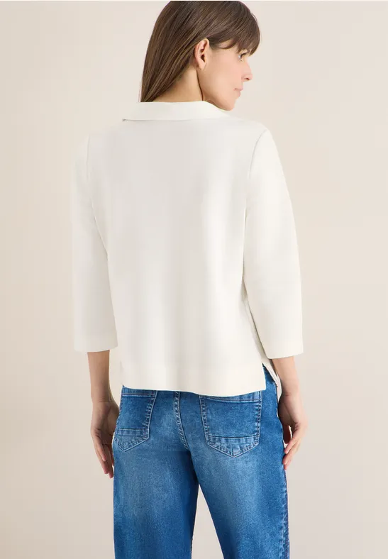 Eine Person trägt einen cremeweißen Pullover mit 3/4-Ärmeln und blaue Jeans, gesehen von hinten.