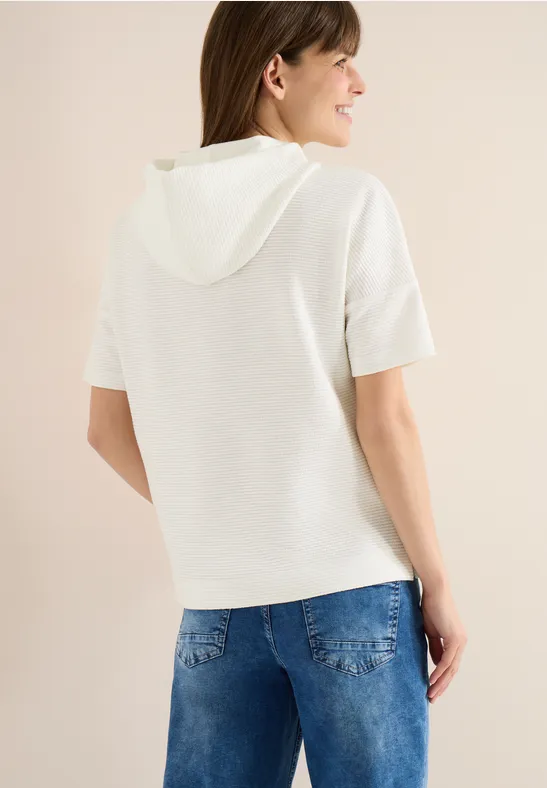 Rückenansicht einer Person in weißem Kurzarm-Kapuzenoberteil und blauen Jeans.