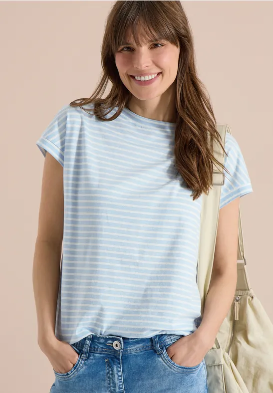 Eine junge Frau trägt ein hellblau-weiß gestreiftes T-Shirt, Jeans und eine beige Stofftasche.