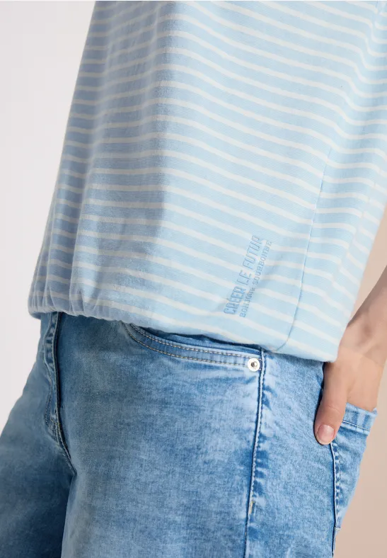 Nahaufnahme einer Person in hellblau-weiß gestreiftem Shirt und blauen Jeans, Hand in Tasche.