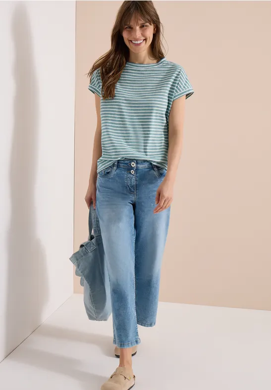 Junge Frau trägt blau-weiß gestreiftes T-Shirt, weite, knöchellange Jeans mit Fransen und hält eine Tasche.