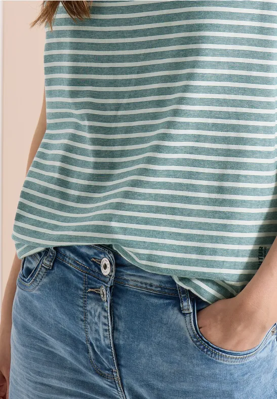 Person in blauer Jeans und hellgrün-weiß gestreiftem Shirt, eine Hand in der Hosentasche.