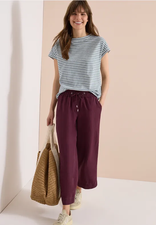 Eine Frau in gestreiftem T-Shirt, lila Hosen und Strohtasche.