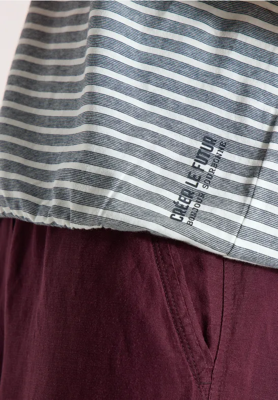 Nahaufnahme eines grauen, weiß gestreiften Oberteils mit Schriftzug und einer weinroten Hose.