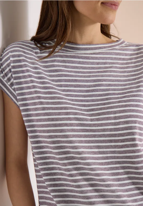 Frau in gestreiftem T-Shirt mit kurzen Ärmeln lehnt an einer Wand.