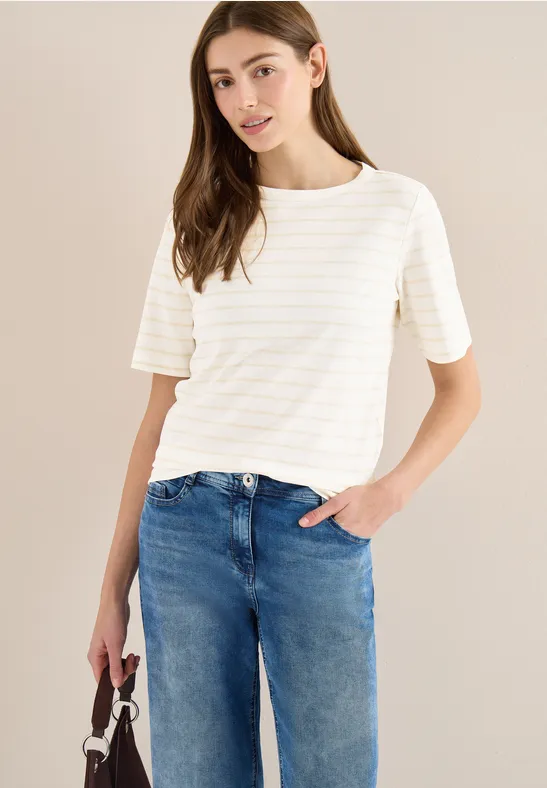 Frau in weißem, gestreiftem Shirt und blauen Jeans trägt eine Tasche und steckt die Hand in die Hosentasche.