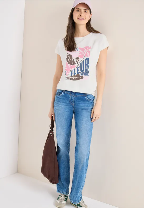 Junge Frau in Schmetterlings-T-Shirt, blauen Jeans, weißen Sneakern und brauner Tasche.