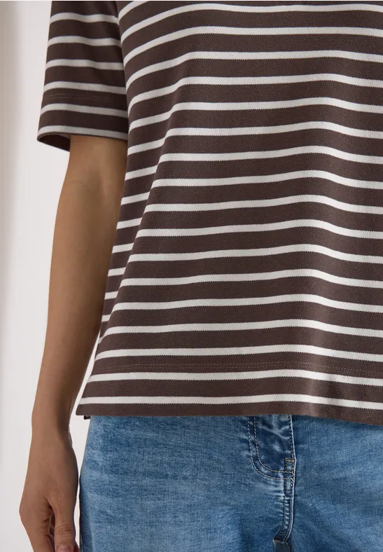 Une personne porte un t-shirt marron et blanc à rayures et un jean bleu.