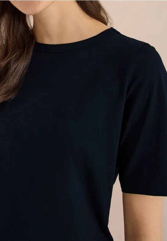 Damenoberkörper mit schwarzem Kurzarmshirt, angedeutetes Lächeln erkennbar.