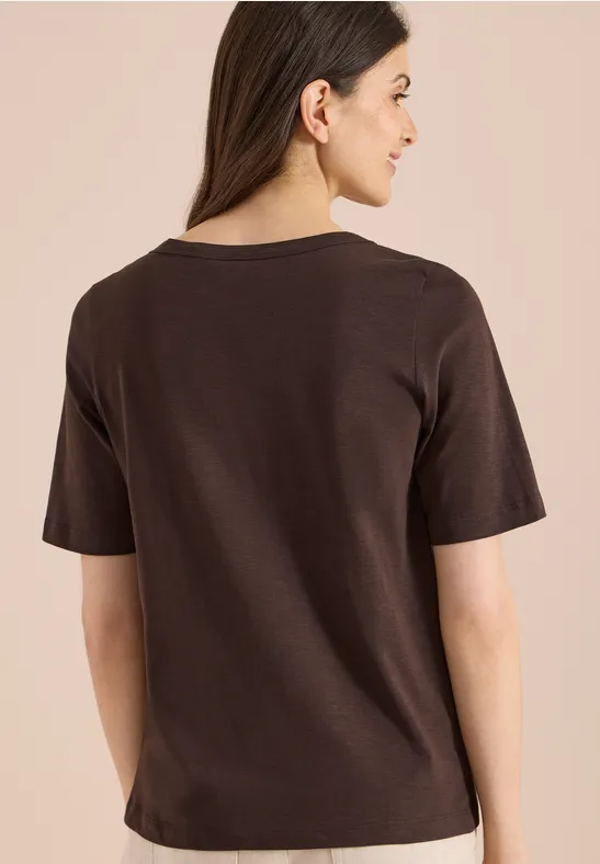 Frau von hinten in schlichtem braunem T-Shirt vor neutralem Hintergrund.