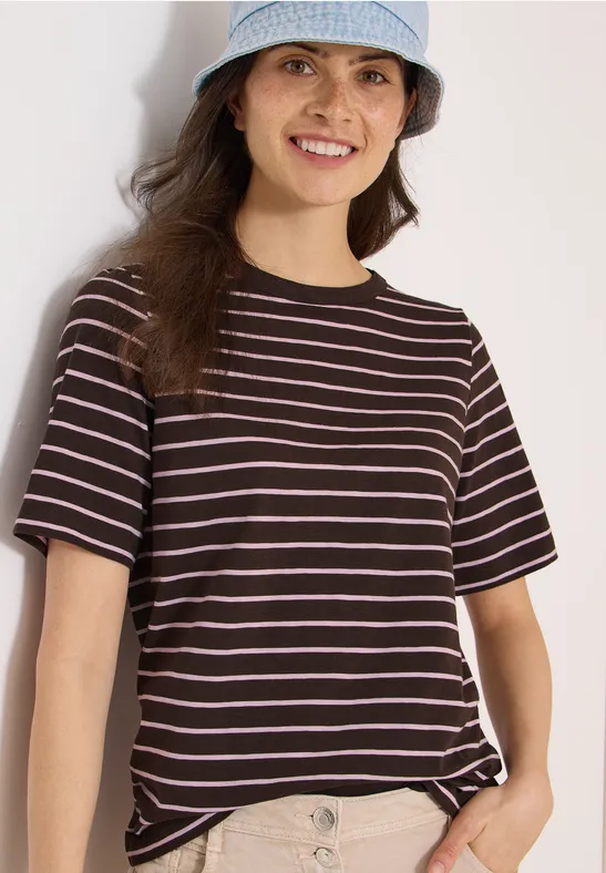 Junge Frau in gestreiftem T-Shirt und Hut steht und hält den Saum des Shirts.