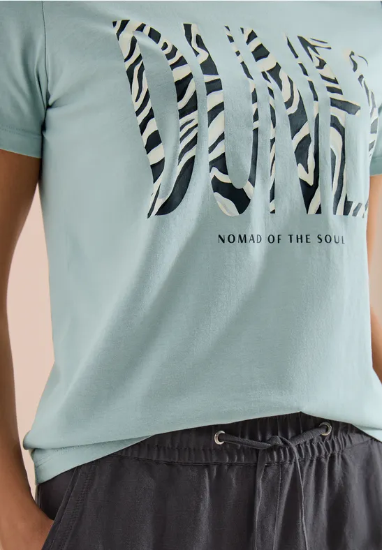 Hellgrünes T-Shirt mit 'DIVE'-Zebra-Print und 'Nomad of the Soul'-Schriftzug, kombiniert mit dunklen Shorts.