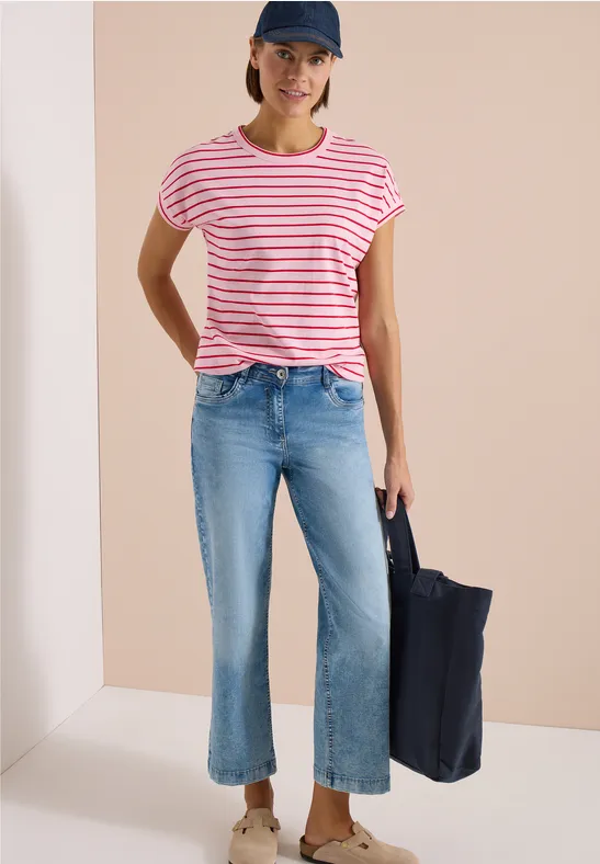 Femme en t-shirt rayé rose et blanc, jean court évasé bleu à fentes, casquette et grand sac bleu marine.