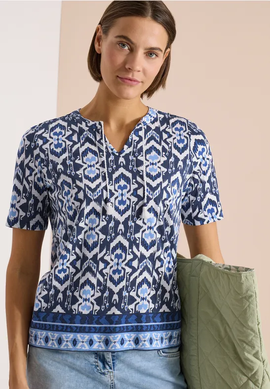 Damen-T-Shirt mit blau-weißem Ethno-Muster, kurzärmelig, kombiniert mit grüner gesteppter Tasche.