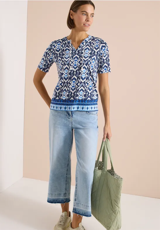 Model trägt blau-weiß gemustertes Shirt, weite Jeans und grüne Stepp-Tasche.