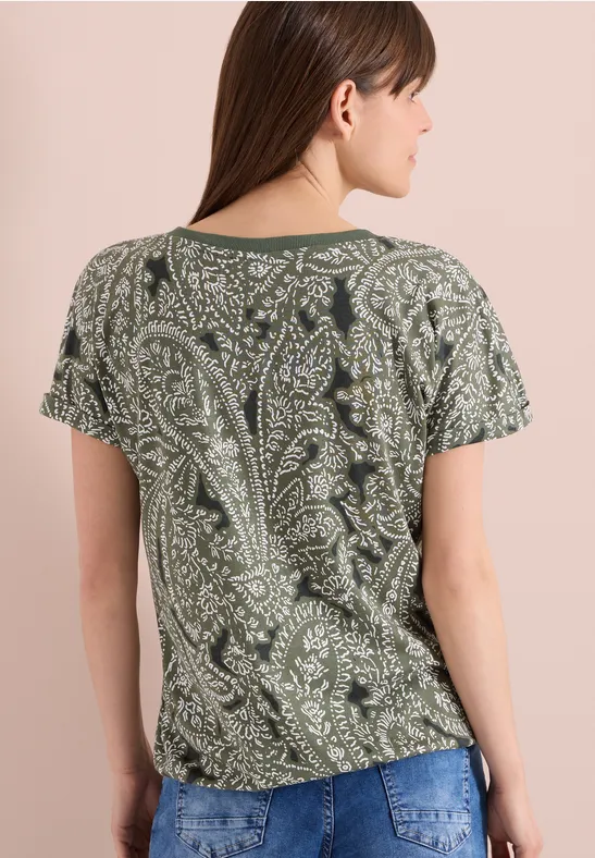 Frau von hinten in olivgrünem T-Shirt mit verspieltem Paisley-Muster und kurzen Ärmeln.
