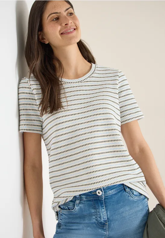 Person trägt ein weißes, gestreiftes T-Shirt und blaue Jeans – legerer Alltagslook.