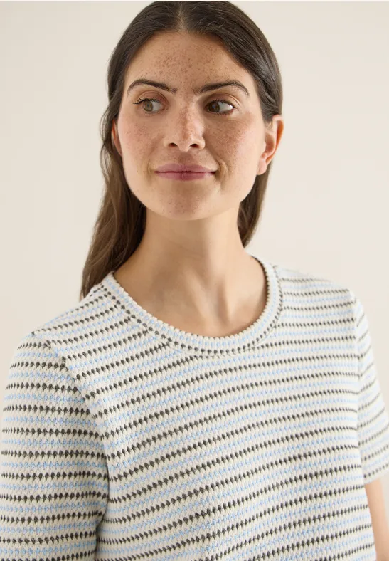 Frau trägt kurzärmliges, weißes T-Shirt mit dünnen grünen Streifen und Rundhalsausschnitt.