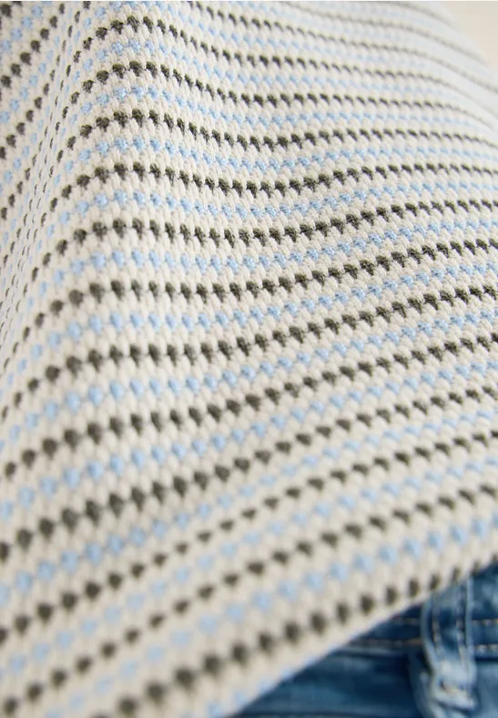 Nahaufnahme eines gestrickten Oberteils mit cremeweißen und hellblauen Streifen über Jeans.