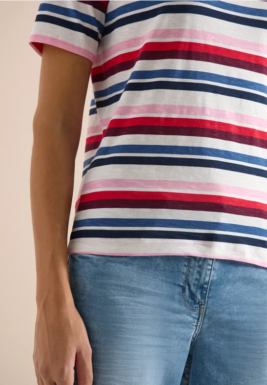 Person in gestreiftem T-Shirt (blau, weiß, rot) und hellen Jeans, Blick auf Oberkörper und Hüfte.