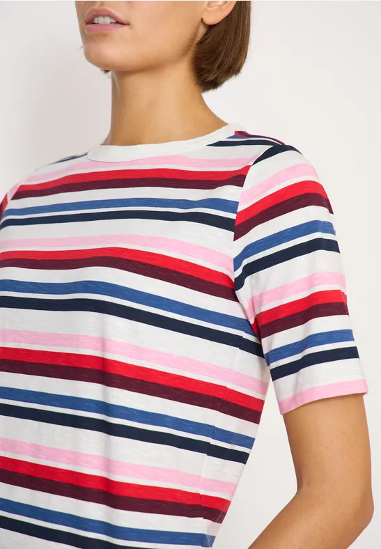 Nahaufnahme einer Frau im T-Shirt mit roten, blauen, weißen und rosa horizontalen Streifen vor weißem Hintergrund.