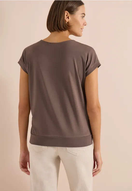 Frau von hinten in locker sitzender kurzer Taupe-Bluse und hellen Hosen, mit kurzem braunem Bob.