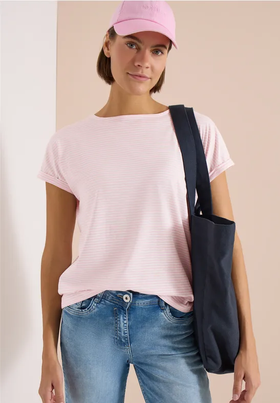 Frau trägt rosa T-Shirt, rosa Cap, blaue Jeans und schwarze Tasche.