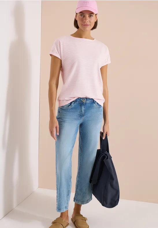 Person in rosa T-Shirt, hellblauen Jeans und großer dunkelblauer Tasche vor hellem Hintergrund.