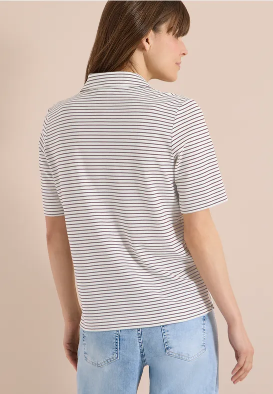 Person von hinten mit gestreiftem Kurzarmshirt und blauen Jeans vor hellem Hintergrund.