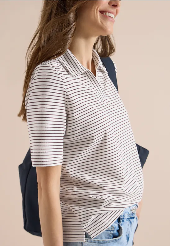 Schwangere Frau in gestreiftem Poloshirt und Jeans mit dunkelblauer Tasche lächelnd seitlich stehend.