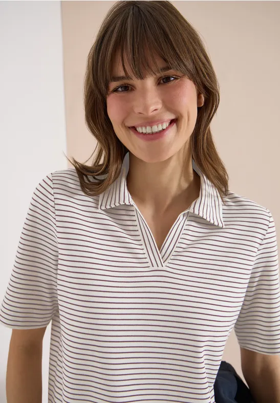 Eine Person mit unscharfem Gesicht trägt ein kurzärmeliges, beige-weiß gestreiftes Poloshirt.