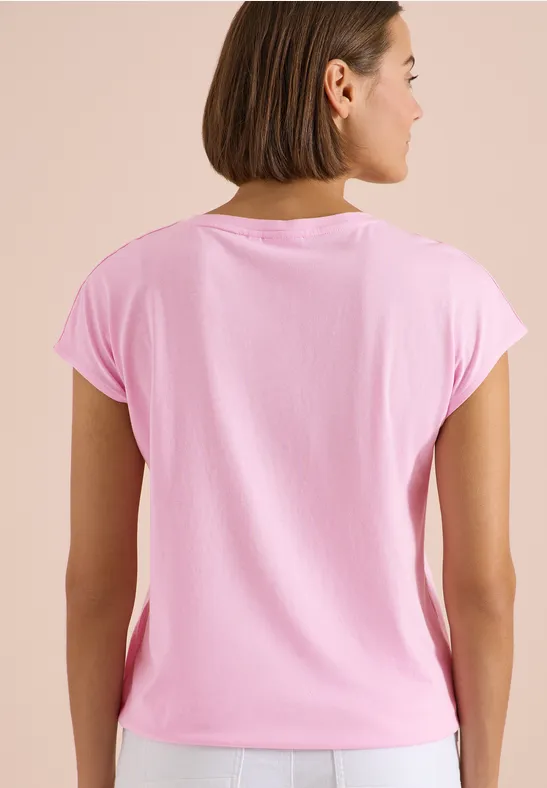 Eine von hinten aufgenommene Frau mit schulterlangem Haar trägt ein hellrosa kurzärmeliges T-Shirt.