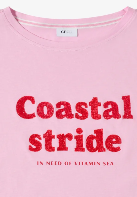 Ein hellrosa T-Shirt mit rotem Glitzerschriftzug 'Coastal stride.' und 'In need of vitamin sea'.