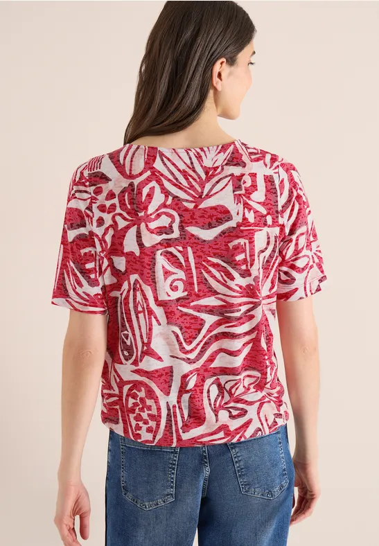 Rückenansicht einer Person in rot-weiß gemustertem Kurzarmshirt und blauer Jeans.