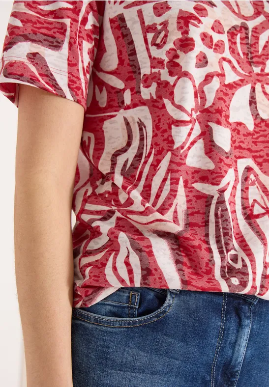 Rotes T-Shirt mit abstrakten weißen Mustern, kombiniert mit einer blauen Jeanshose.