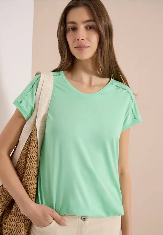 Frau trägt mintgrünes T-Shirt und hält eine große geflochtene Tasche.