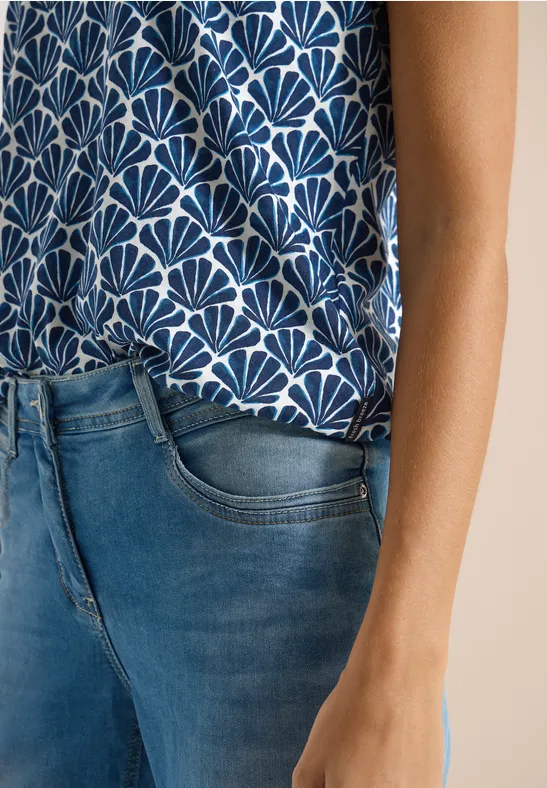 Eine Person trägt eine gemusterte ärmellose Bluse und eine blaue Jeans.