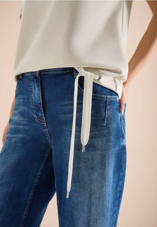 Nahaufnahme einer Person in blauen Jeans und weißem Top, Hände in den Taschen.