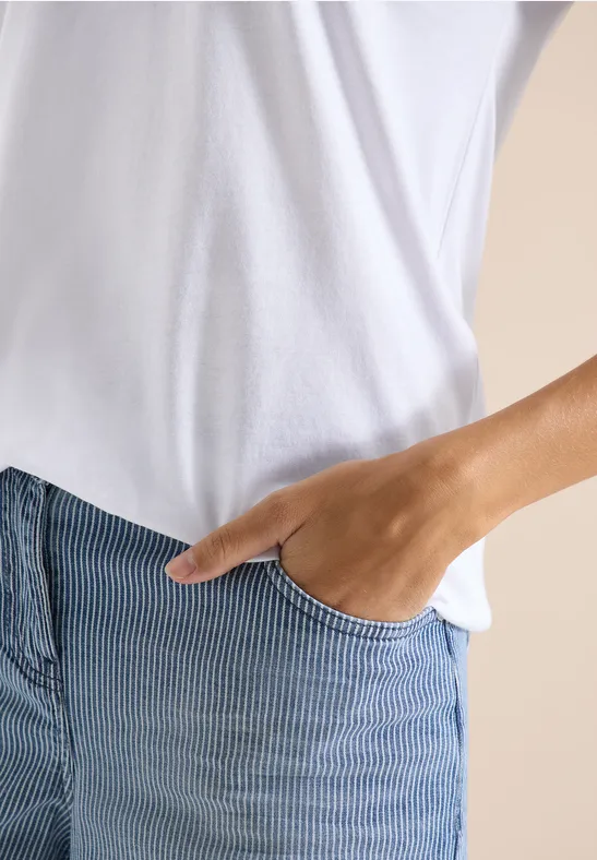 Eine Person in weißem T-Shirt und blauen, gestreiften Shorts mit einer Hand in der Tasche.