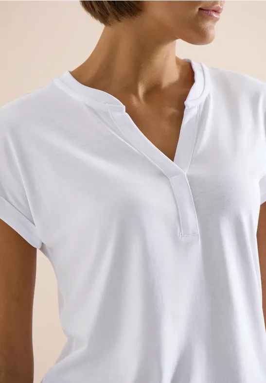 Oberkörper einer Frau in weißem, kurzärmeligen Shirt mit V-Ausschnitt und Stehkragen.