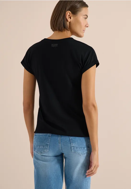 Rückansicht einer Person in schwarzem T-Shirt und hellblauen Jeans vor neutralem Hintergrund.