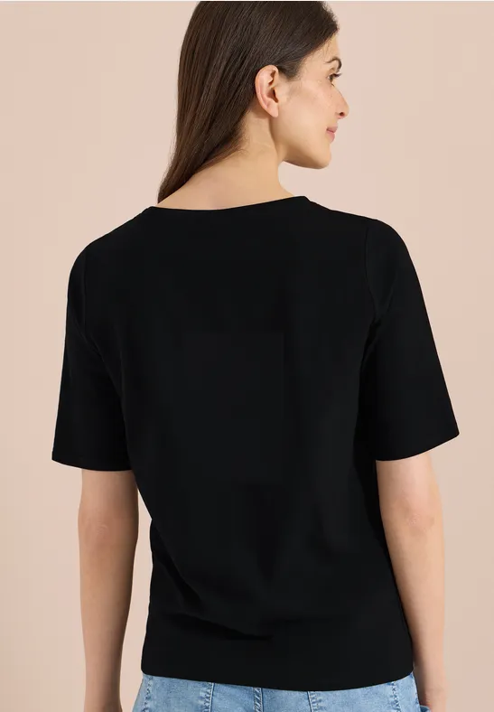 Frau von hinten in schlichtem schwarzen T-Shirt vor neutralem Hintergrund.