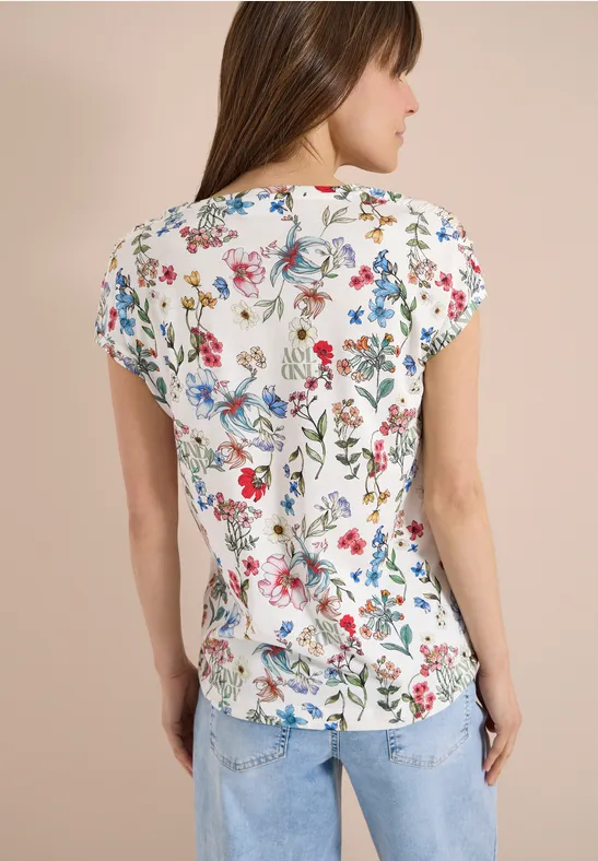 Frau von hinten in weißem Shirt mit buntem Blumenmuster und blauen Jeans.