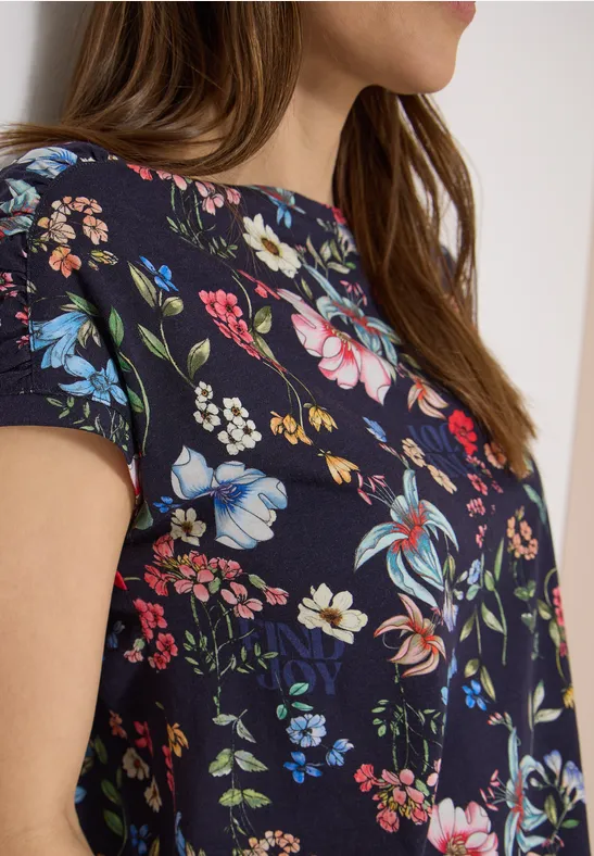 Seitliche Ansicht einer Frau in marineblauer Bluse mit buntem Blumenmuster.