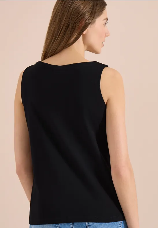 Vue de dos d’une femme portant un haut sans manches noir sur fond clair.